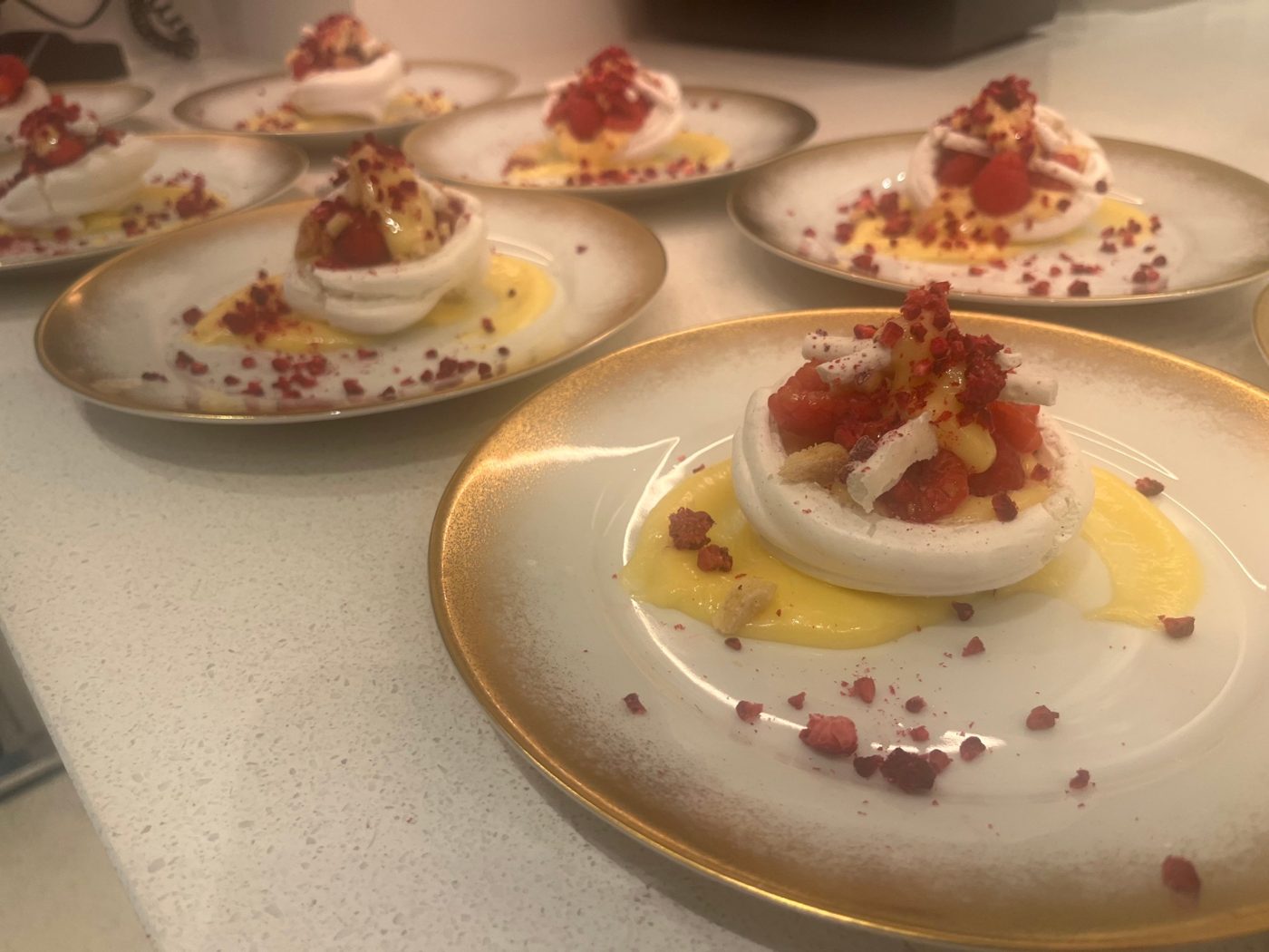 Individual pavlovas with lemon curd and raspberries on gold plates by chef Troy Davidson